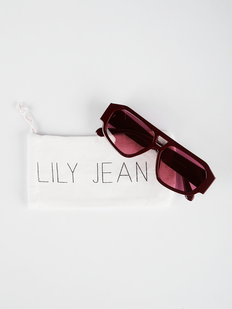 Rectangle sunglasses in deep wine frame with pink-tinted lenses on white packaging pouch by Lily Jean
