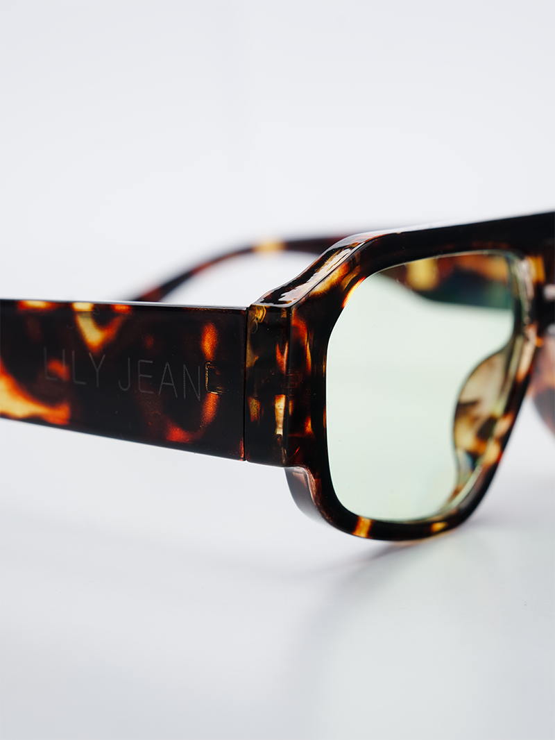 Oversized rectangle sunglasses with a dark brown and amber tortoiseshell frame and tinted light green lenses - close-up view
