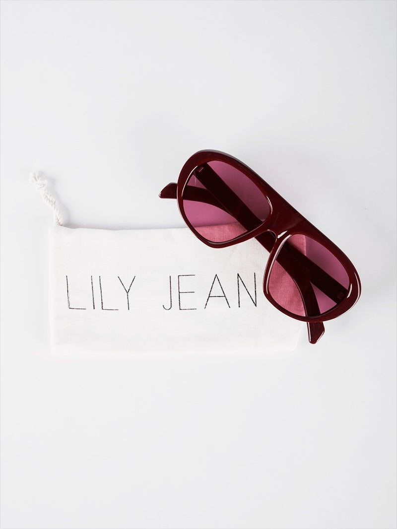 Square-aviator sunglasses in deep wine with dark gray lenses on a white drawstring packaging pouch by Lily Jean